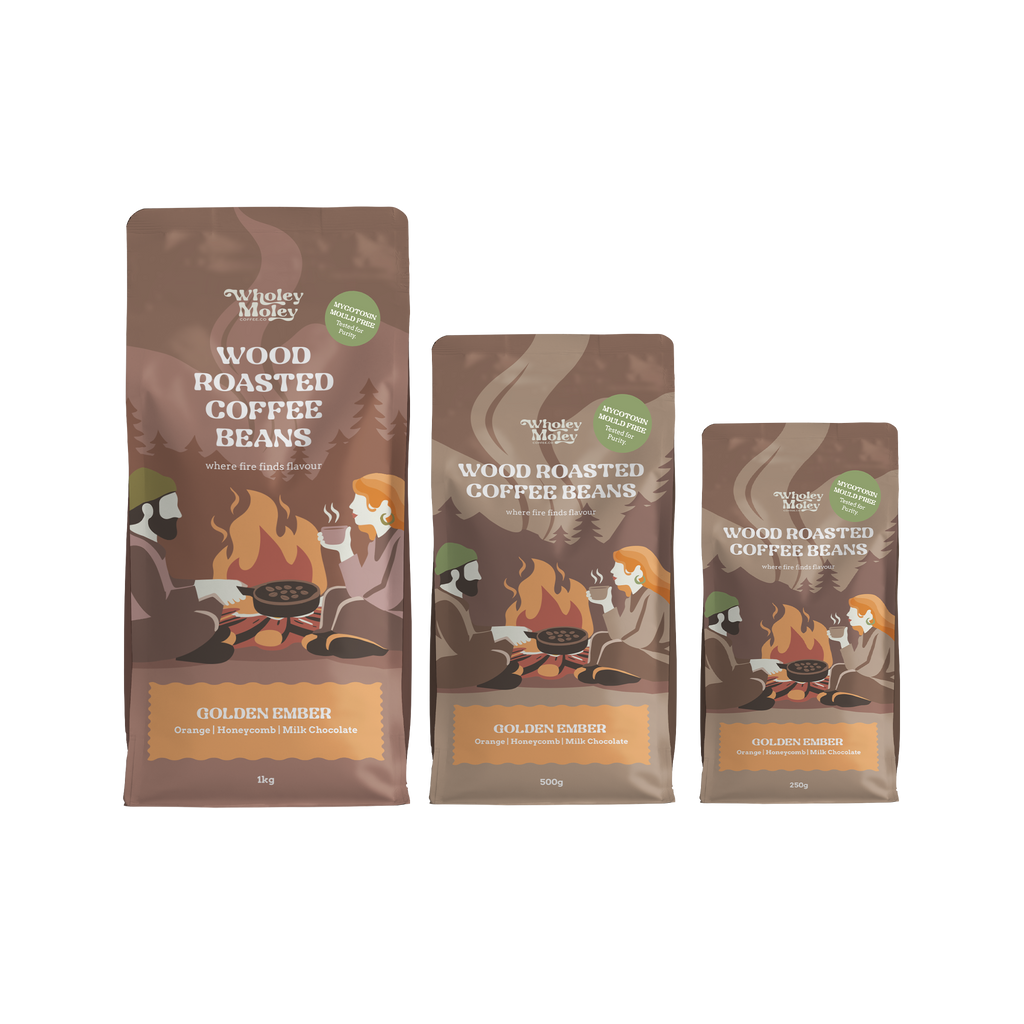 Three bags of Wholey Moley Wood Roasted Coffee Beans in different sizes: The bags are brown with illustrations of campers around campfires and a green circular badge.