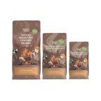 Three bags of Wholey Moley Wood Roasted Coffee Beans in different sizes: The bags are brown with illustrations of campers around campfires and a green circular badge.